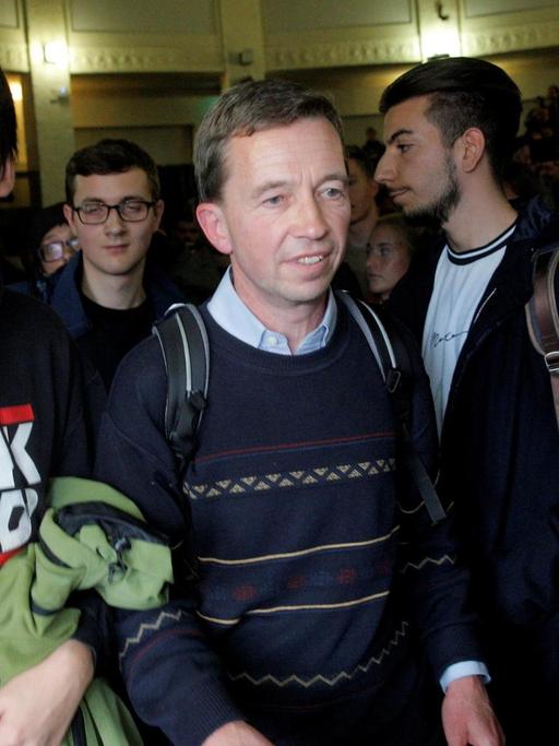 Bernd Lucke drängt sich nach seiner verhinderten Vorlesung aus dem Saal. Neben ihm ein Demonstrant in einem Pullover mit der Aufschrift "FCK AFD".