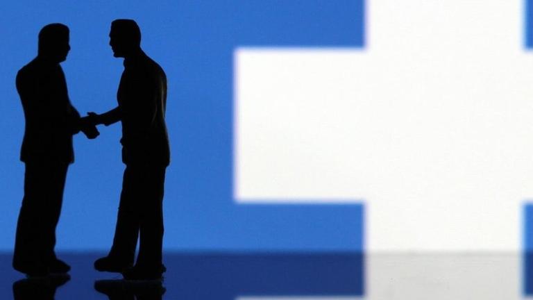 Miniaturfiguren geben sich die Hand vor einem Facebook-Logo. Miniaturfiguren geben sich die Hand vor einem Facebook-Logo.