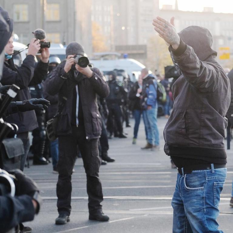 07.11.2020, Sachsen, Leipzig: Teilnehmer der Demonstration der Initiative ?Querdenken? rufen und gestikulieren mit ausgebreiteten Armen auf dem Augustusplatz vor Medienvertretern und Polizisten. An der Kundgebung gegen die von Bund und Ländern beschlossenen Corona-Maßnahmen nehmen mehrere Tausend Menschen teil. Foto: Sebastian Willnow/dpa-Zentralbild/dpa | Verwendung weltweit