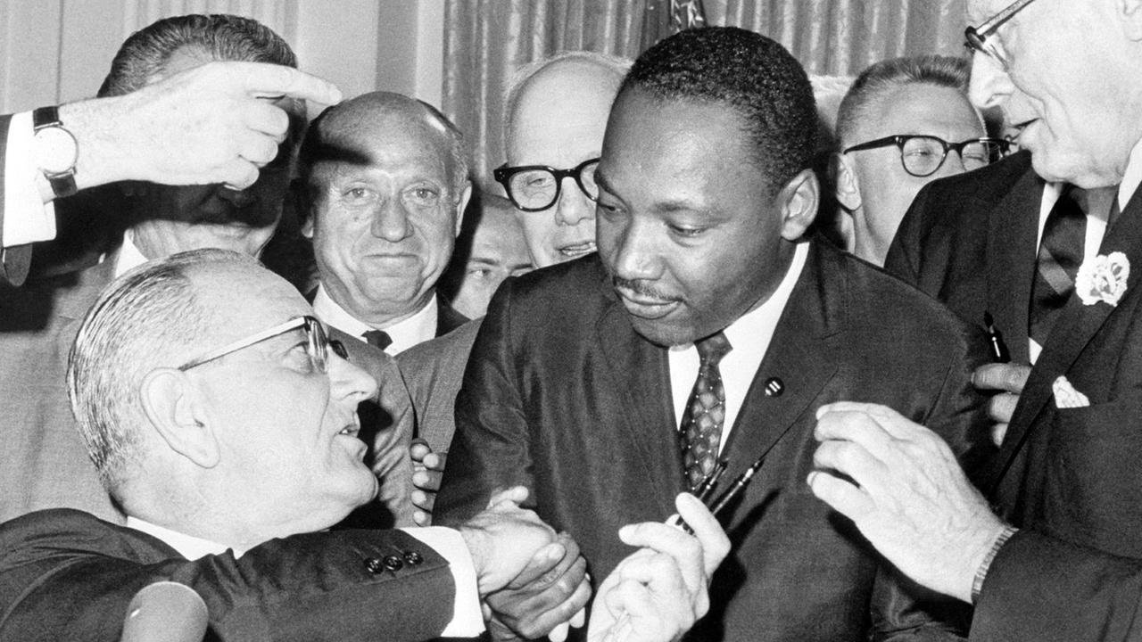 Nach der Unterzeichnung des Bürgerrechts-Gesetzes am 2.7.1964 in Washington DC. reicht US-Präsident Lyndon Baines Johnson (l) den Federhalter an den Bürgerrechtler Martin Luther King weiter und gibt ihm die Hand. Das Bürgerrechtsgesetz sollte eine Gleichberechtigung der farbigen Bevölkerung in den Vereinigten Staaten von Amerika garantieren und galt als eine der wichtigsten Gesetzes-Entscheidungen in der Geschichte der USA. King wurde am 4.4.1968 im Alter von 39 Jahren in Memphis von James Earl Ray erschossen. Nach der Unterzeichnung des Bürgerrechts-Gesetzes am 2.7.1964 in Washington DC. reicht US-Präsident Lyndon Baines Johnson (l) den Federhalter an den Bürgerrechtler Martin Luther King weiter und gibt ihm die Hand. Das Bürgerrechtsgesetz sollte eine Gleichberechtigung der farbigen Bevölkerung in den Vereinigten Staaten von Amerika garantieren und galt als eine der wichtigsten Gesetzes-Entscheidungen in der Geschichte der USA. King wurde am 4.4.1968 im Alter von 39 Jahren in Memphis von James Earl Ray erschossen.
