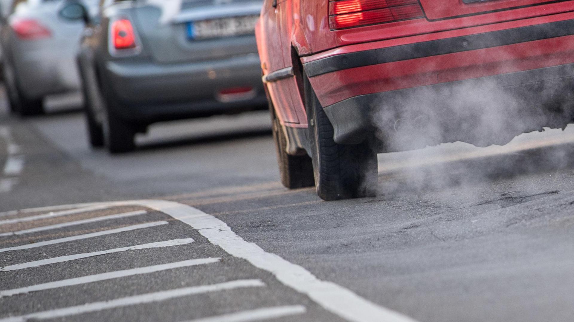 Rückansicht von Autos, die durch die Stadt fahren. Bei hintersten Auto sind die Abgase aus dem Auspuff deutlich zu sehen. Rückansicht von Autos, die durch die Stadt fahren. Bei hintersten Auto sind die Abgase aus dem Auspuff deutlich zu sehen.
