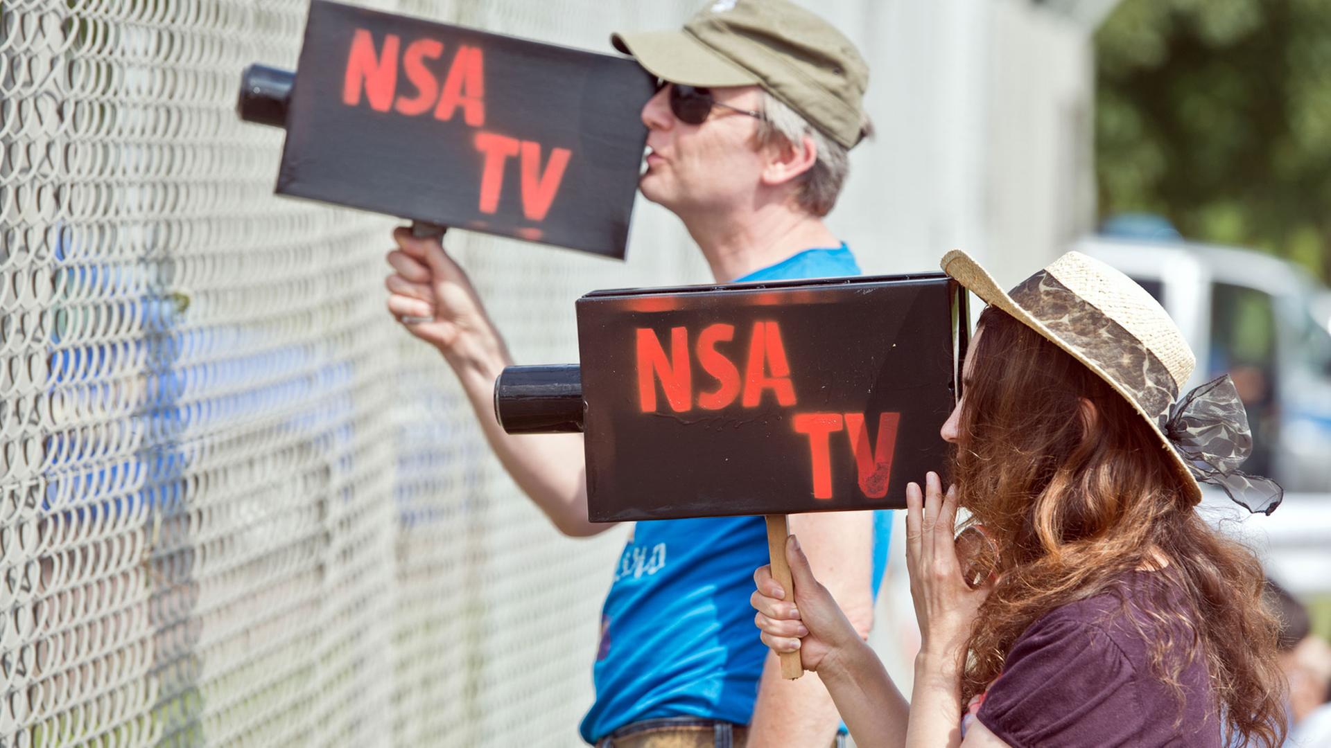 Mit zwei Pappkameras mit der Aufschrift "NSA TV" schauen zwei Teilnehmer einer Protestkundgebung vor dem "Dagger Complex" des US-Geheimdiensts NSA in Griesheim bei Darmstadt (Hessen) am 26.07.2014 durch den Sicherheitszaun der Anlage. Mit zwei Pappkameras mit der Aufschrift "NSA TV" schauen zwei Teilnehmer einer Protestkundgebung vor dem "Dagger Complex" des US-Geheimdiensts NSA in Griesheim bei Darmstadt (Hessen) am 26.07.2014 durch den Sicherheitszaun der Anlage.
