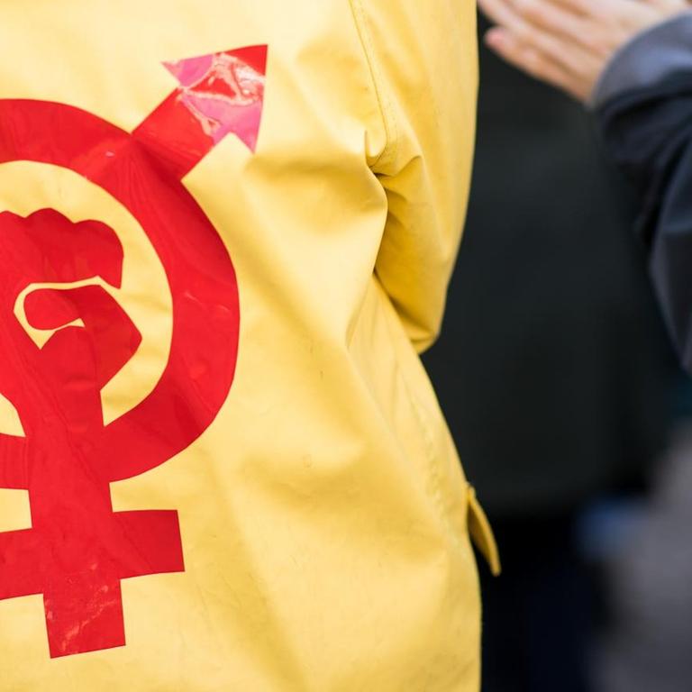 Eine Frau trägt einen gelben Regenmantel mit einem roten Gender- und Protestsymbol bei einer Kundgebung zum Internationalen Frauentag vor dem Rathaus in Hamburg.