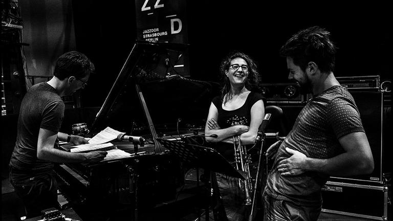 Auf dem schwarz/weiß Foto sind eine Musikerin und zwei Musiker zu sehen, die für den Auftritt beim Jazzdor Festival proben Auf dem schwarz/weiß Foto sind eine Musikerin und zwei Musiker zu sehen, die für den Auftritt beim Jazzdor Festival proben