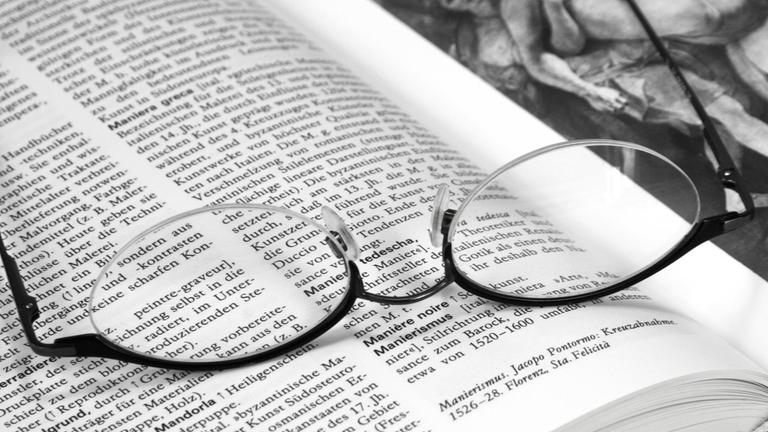 Auf einem aufgeschlagenen Kunstlexikon liegt eine Brille