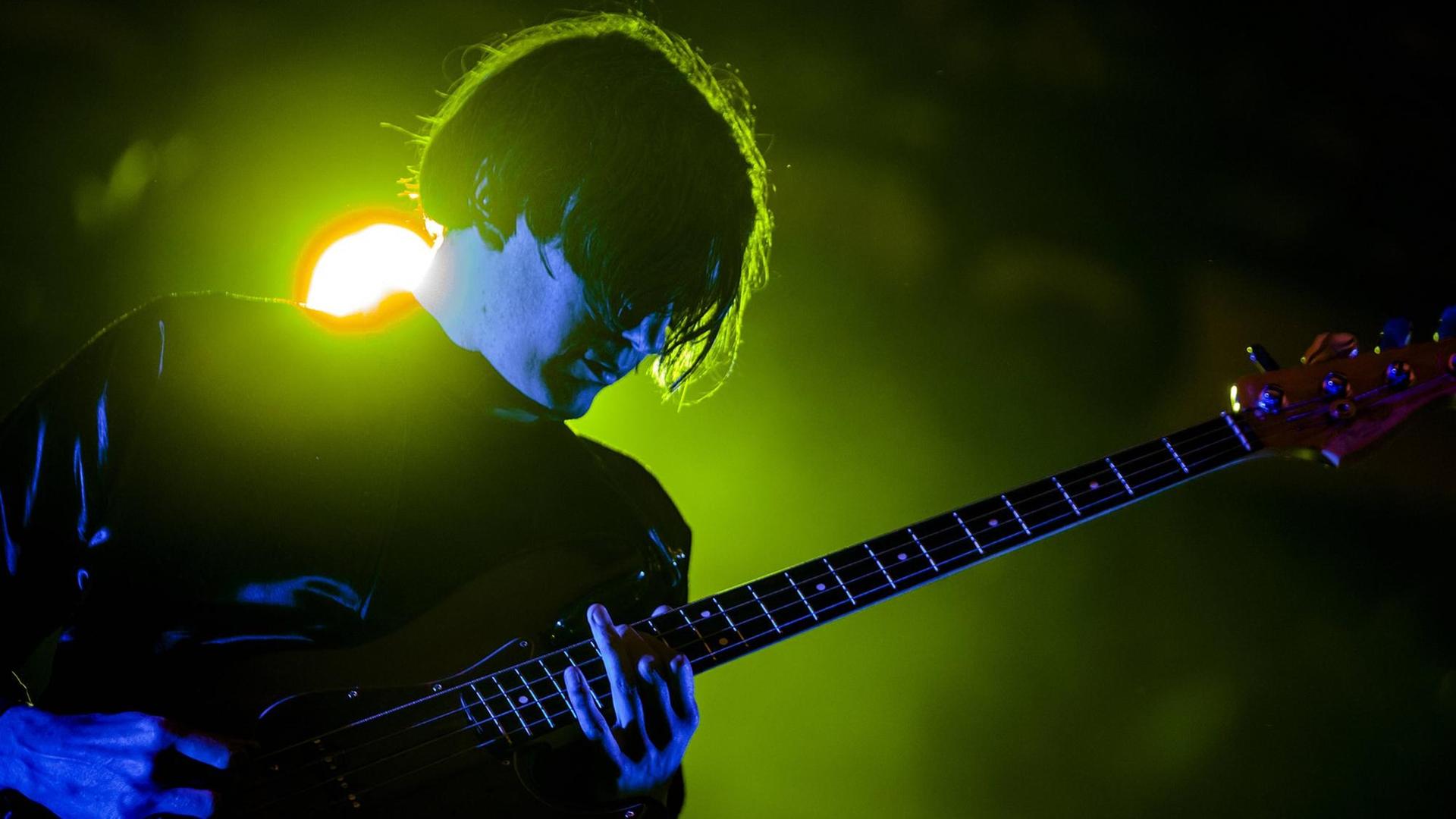 Nikolai Fraiture steht vor einem grell grünen Scheinwerfer und spielt Gitarre bei einem Auftritt von "The Strokes". Nikolai Fraiture steht vor einem grell grünen Scheinwerfer und spielt Gitarre bei einem Auftritt von "The Strokes".