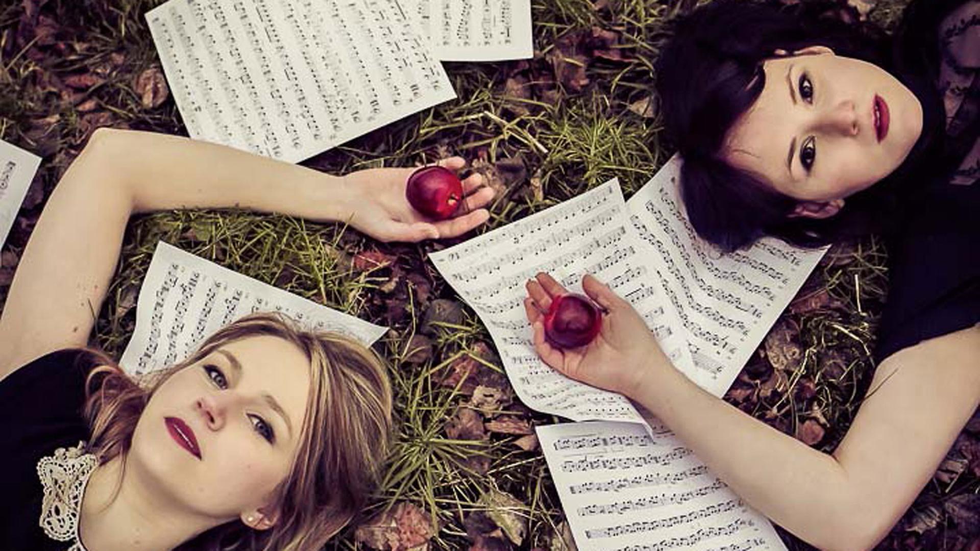 Zwei junge Frauen liegen - je mit einem Apfel in der Hand - auf verstreuten Notenblätter im Gras. Zwei junge Frauen liegen - je mit einem Apfel in der Hand - auf verstreuten Notenblätter im Gras.