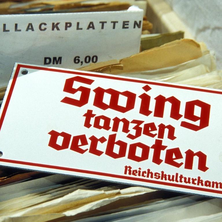 Ein Schild mit der Aufschrift "Swing tanzen verboten - Reichskulturkammer" liegt auf Schellackplatten auf einem Flohmarkt