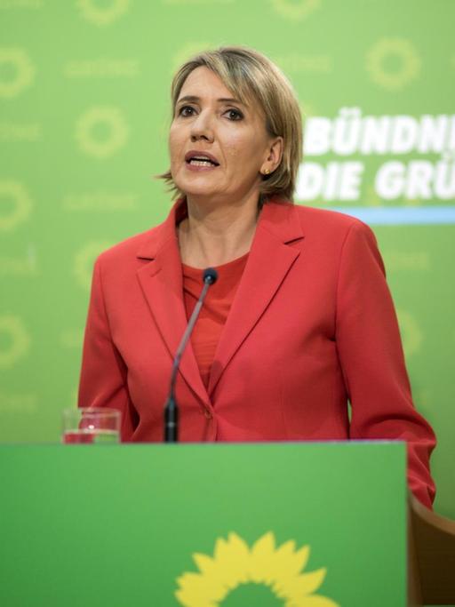 Simone Peter spricht bei einer Pressekonferenz, im Hintergrund das Parteilogo der Grünen.