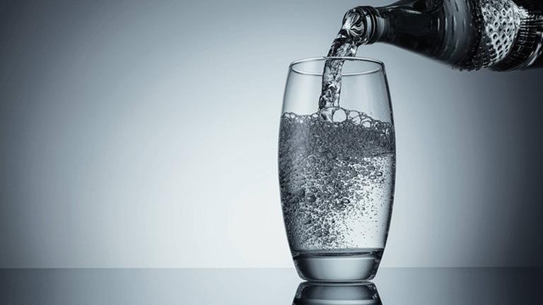 Wasser wird aus der Flasche in ein Glas eingeschenkt Wasser wird aus der Flasche in ein Glas eingeschenkt