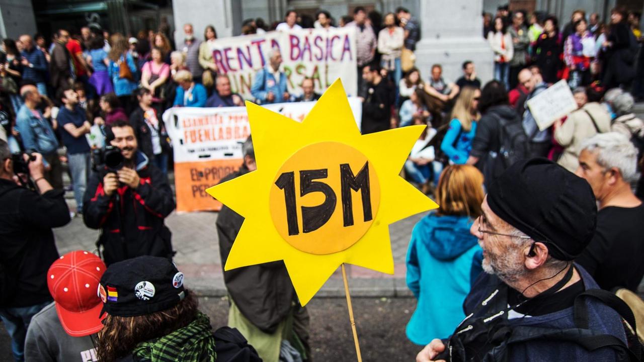 Demonstranten mit einem Schild in Form einer Sonne und mit der Aufschrift "15M". Demonstranten mit einem Schild in Form einer Sonne und mit der Aufschrift "15M".