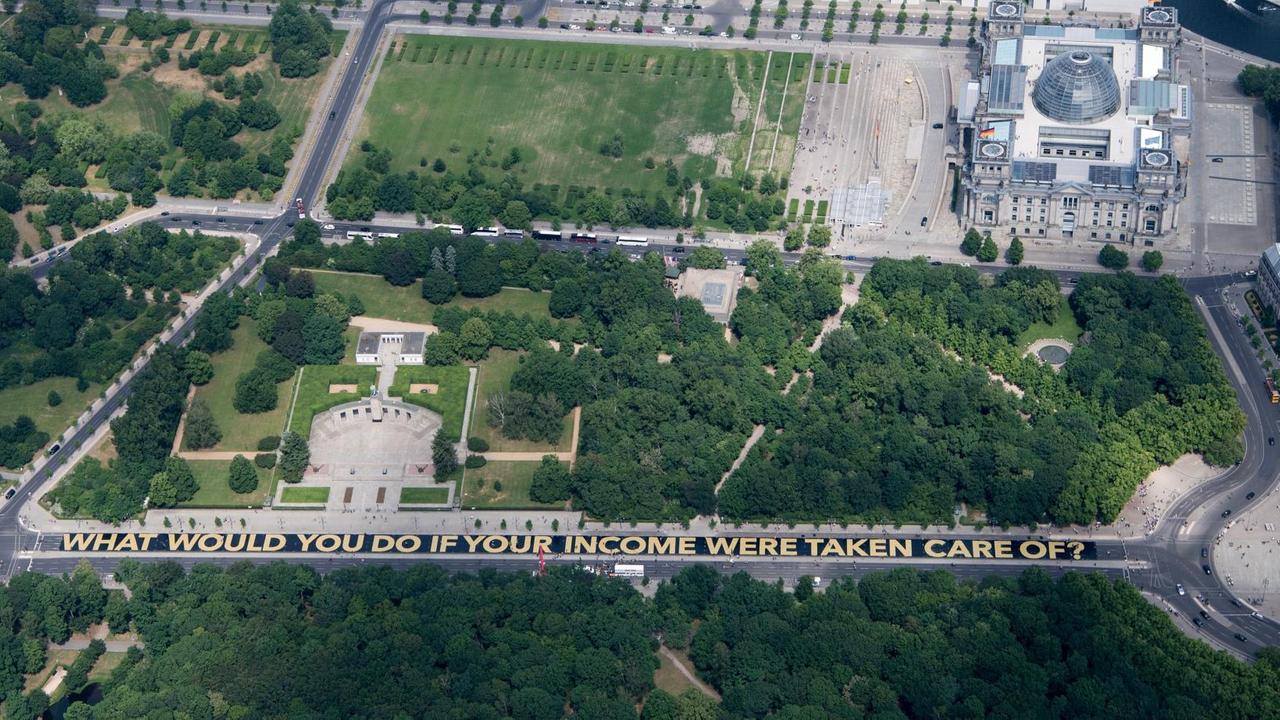 "WHAT WOULD YOU DO IF YOUR INCOME WERE TAKEN CARE OF?" steht am 29.05.2016 auf riesigen Plakaten auf der Straße des 17. Juni zwischen der Siegessäule und dem Brandenburger Tor in Berlin. "WHAT WOULD YOU DO IF YOUR INCOME WERE TAKEN CARE OF?" steht am 29.05.2016 auf riesigen Plakaten auf der Straße des 17. Juni zwischen der Siegessäule und dem Brandenburger Tor in Berlin.