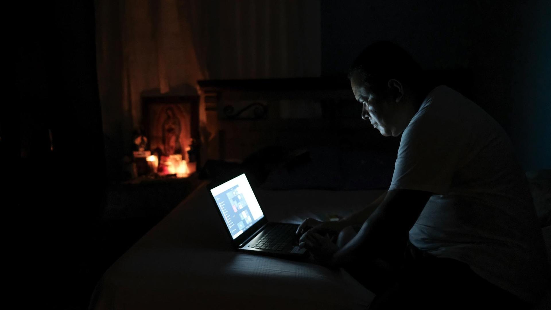 Ein Mann sitzt im Dunkeln und arbeitet an einem Laptop, der noch Strom hat. Ein Mann sitzt im Dunkeln und arbeitet an einem Laptop, der noch Strom hat.