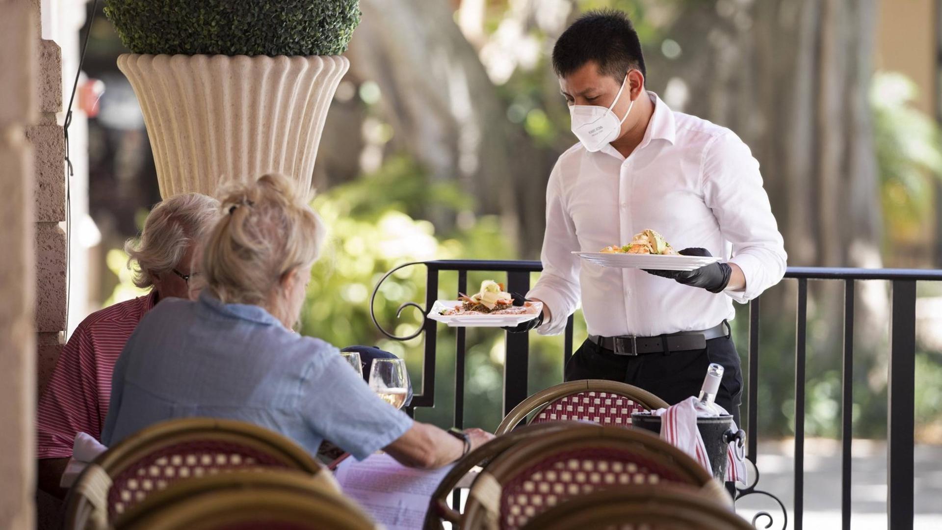 Ein Kellner serviert mit Mundschutz in einem Restaurant Essen. Ein Kellner serviert mit Mundschutz in einem Restaurant Essen.