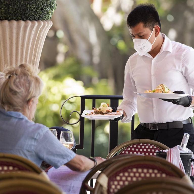 Ein Kellner serviert mit Mundschutz in einem Restaurant Essen.