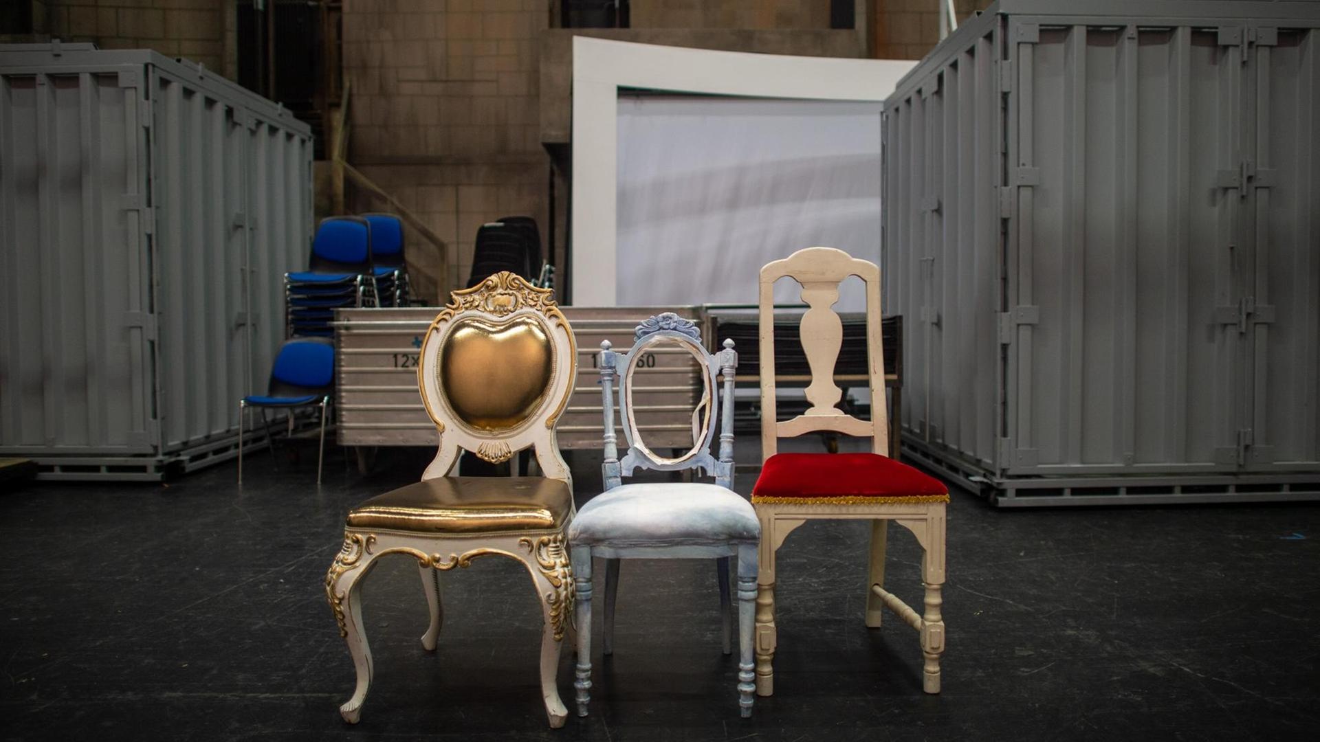 Drei Requisiten-Stühle stehen nebeneinander im Opernhaus des Theaters Magdeburg hinter der Bühne. Im Hintergrund sind Container zu sehen. Drei Requisiten-Stühle stehen nebeneinander im Opernhaus des Theaters Magdeburg hinter der Bühne. Im Hintergrund sind Container zu sehen.