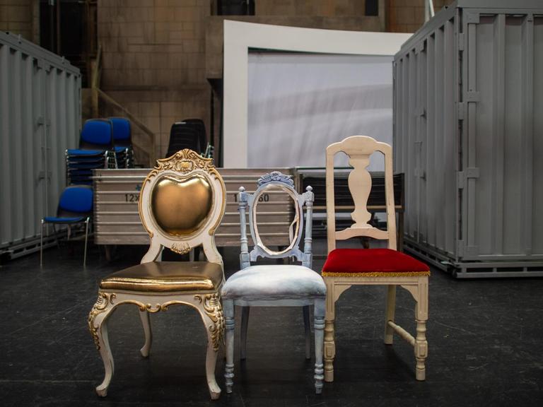 Drei Requisiten-Stühle stehen nebeneinander im Opernhaus des Theaters Magdeburg hinter der Bühne. Im Hintergrund sind Container zu sehen.
