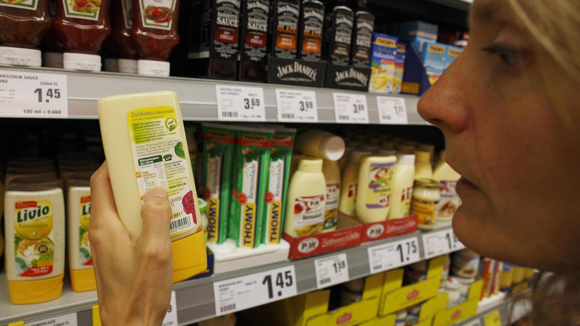 Eine kritische Verbraucherin studiert die Angaben auf einer Mayonnaise Verpackung. Eine kritische Verbraucherin studiert die Angaben auf einer Mayonnaise Verpackung.