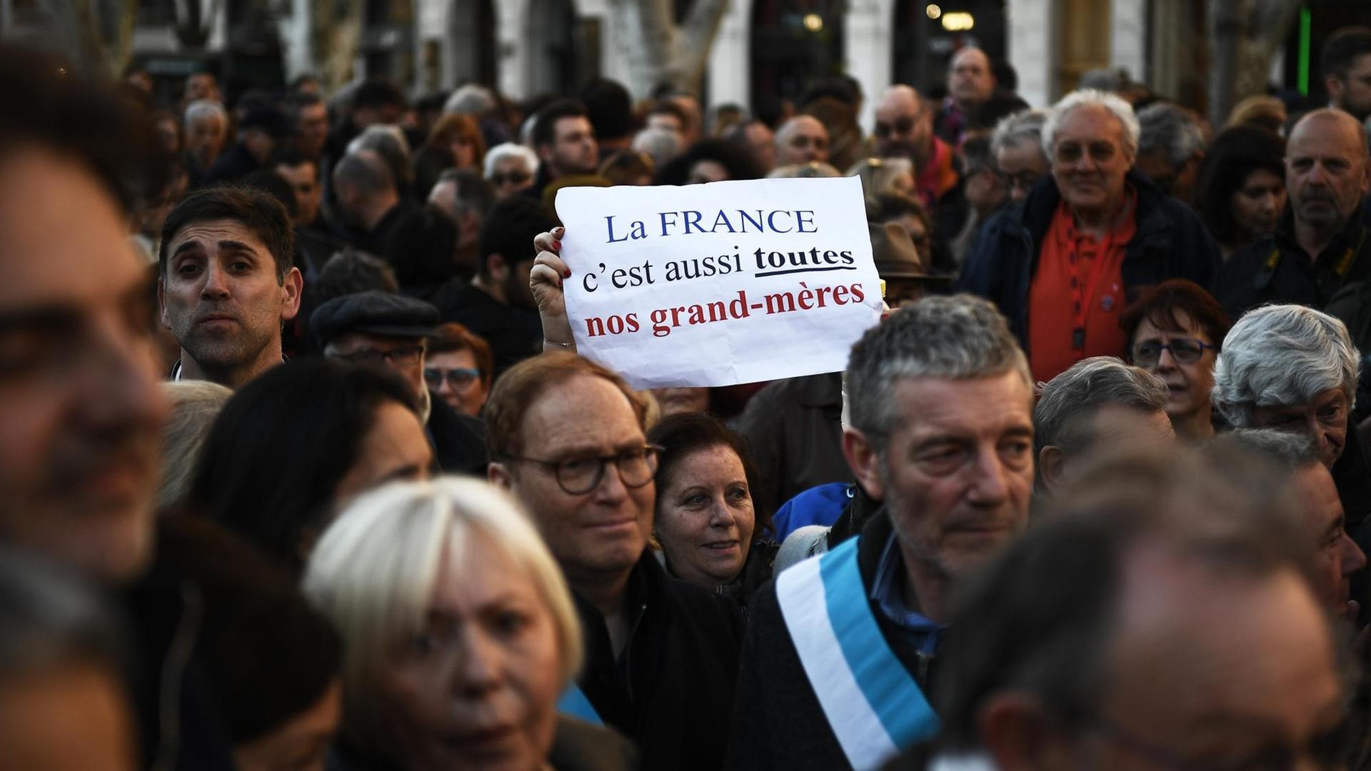 "Frankreich, das sind auch unsere Großeltern", steht auf einem Plakat einer Demonstrantin in Marseille. Sie steht in einer Menschenmenge.