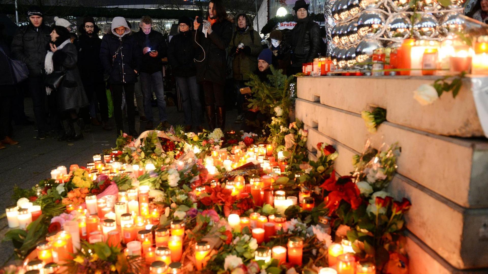 Menschen stehen in der Dunkelheit hinter einem Meer aus Kerzen und Blumen neben einer Beton-Absperrung. Menschen stehen in der Dunkelheit hinter einem Meer aus Kerzen und Blumen neben einer Beton-Absperrung.