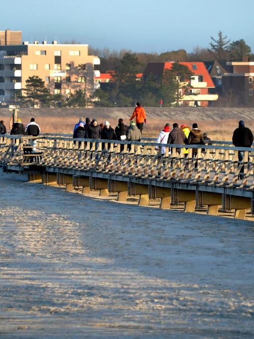 Touristen gehen über die Seebrücke am Strand in Sankt Peter-Ording.