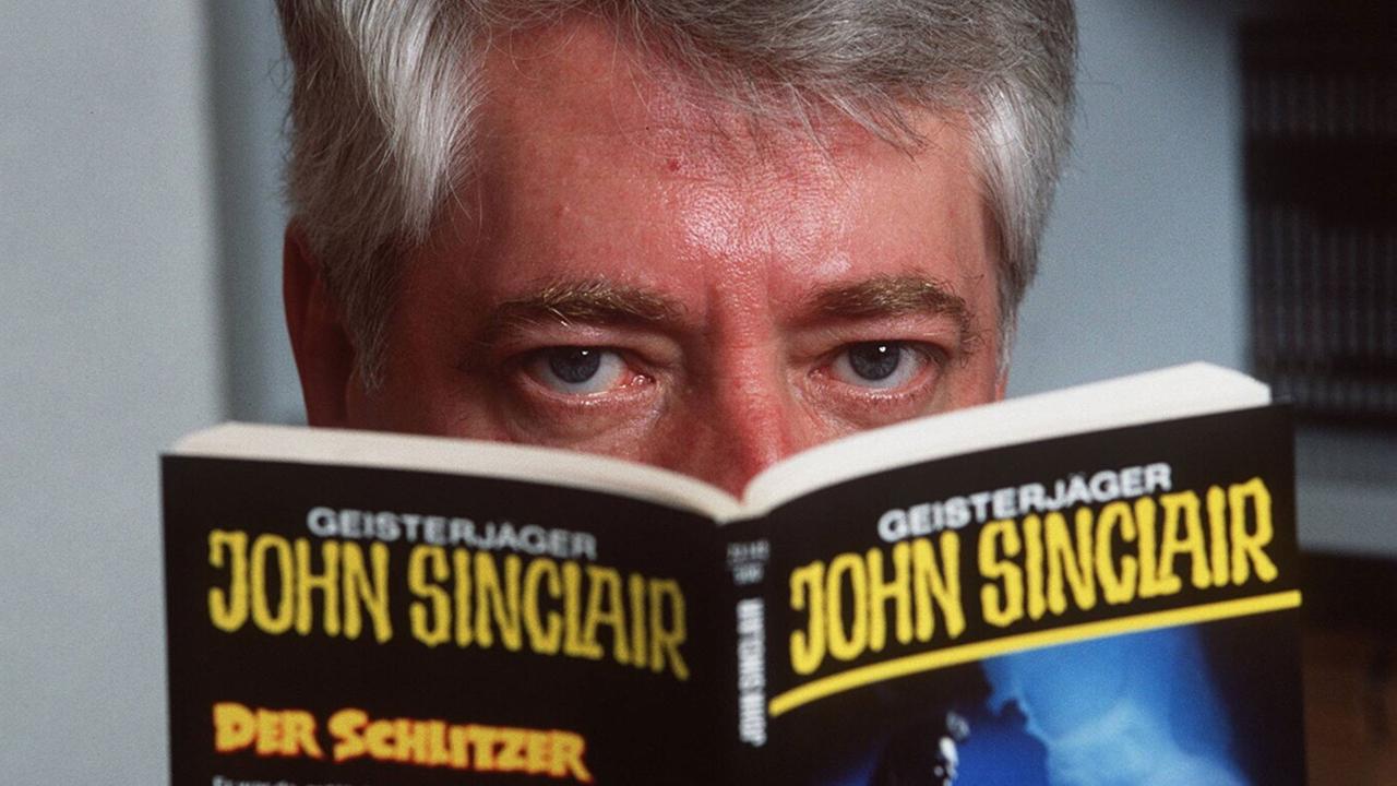 Der Autor Helmut Rellergerd alias Jason Dark hinter einem seiner Heftromane. Auf dem Titel steht "Geisterjäger John Sinclair. Der Schlitzer"