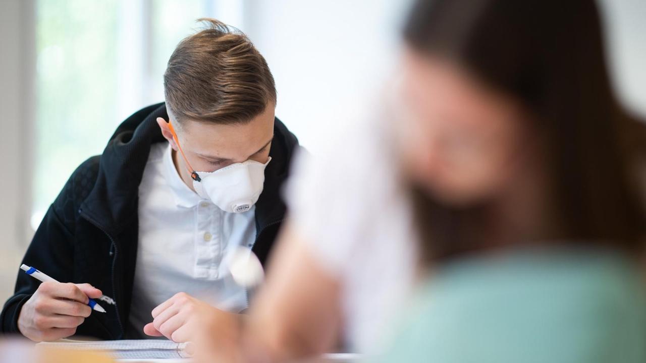 Schülerinnen und Schüler, einer davon mit einer Schutzmaske, bearbeiten Informatikaufgaben. Schülerinnen und Schüler, einer davon mit einer Schutzmaske, bearbeiten Informatikaufgaben.