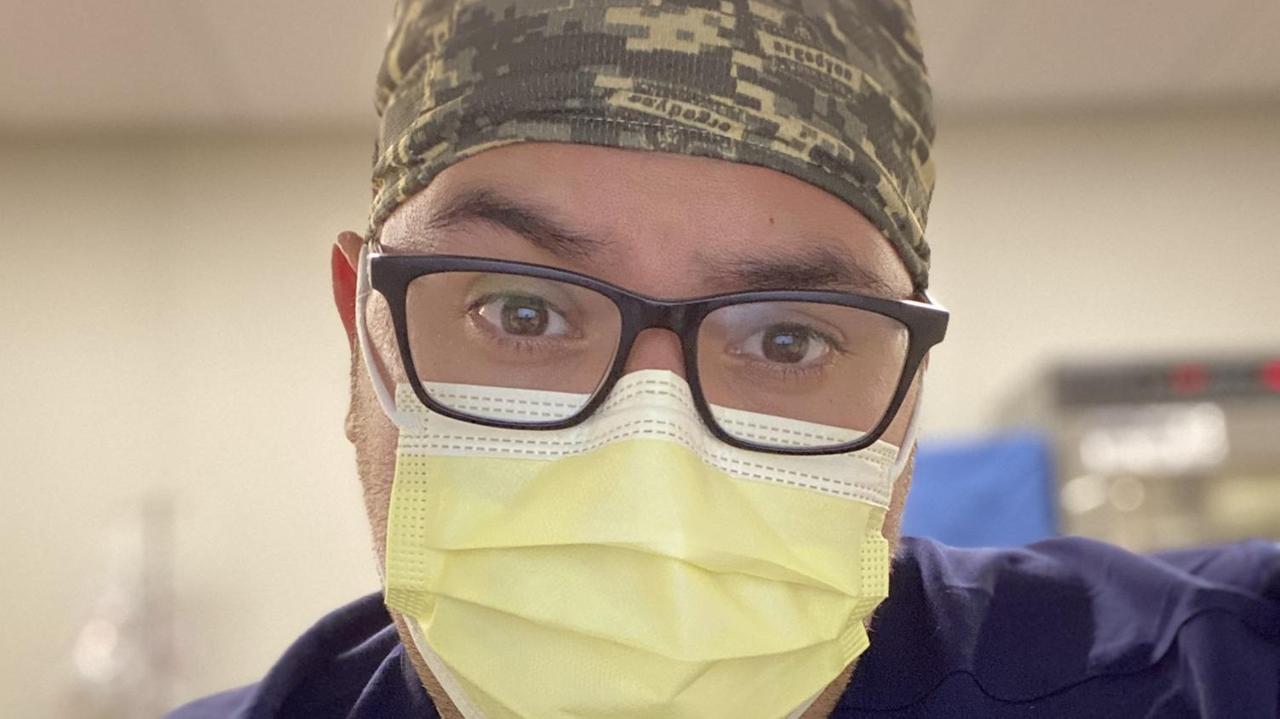 Ein junger Mann mit gelbem Mundschutz, Brille und einem blauen Kittel. Ein junger Mann mit gelbem Mundschutz, Brille und einem blauen Kittel.
