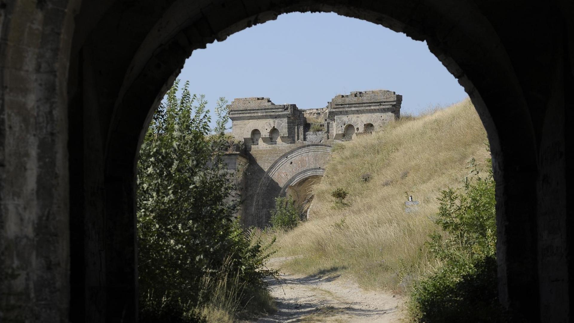 Blick durch einen Tunnel auf die Festung "Fort Totleben": Ein steinernder Torbogen, umgeben von Wiese und Gebüschen. 