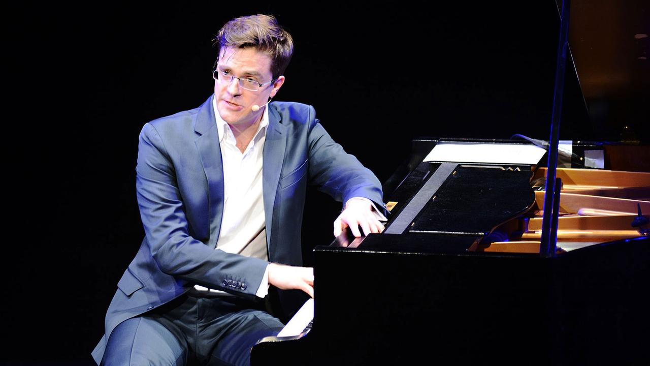 Bodo Wartke in blauem Anzug und weißem Hemd sitzt seitlich am Klavier zum Publikum gewandt Bodo Wartke in blauem Anzug und weißem Hemd sitzt seitlich am Klavier zum Publikum gewandt