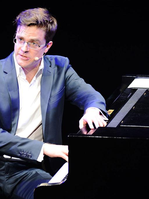 Bodo Wartke in blauem Anzug und weißem Hemd sitzt seitlich am Klavier zum Publikum gewandt