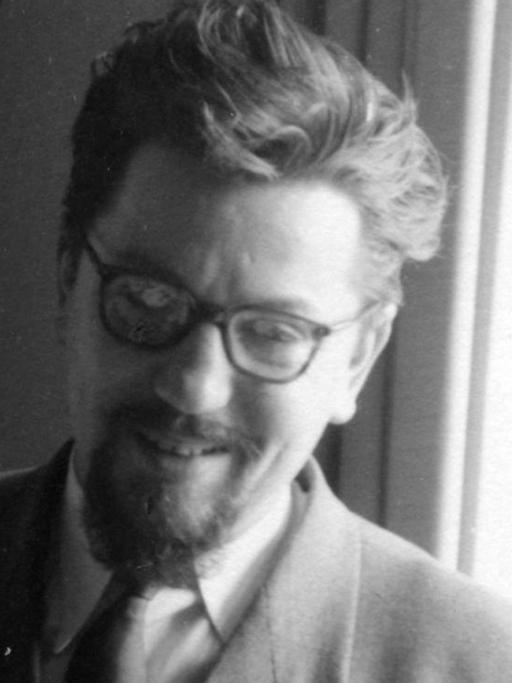 Der Komponist Bernd Alois Zimmermann steht vor einem Fenster, raucht und lächelt.