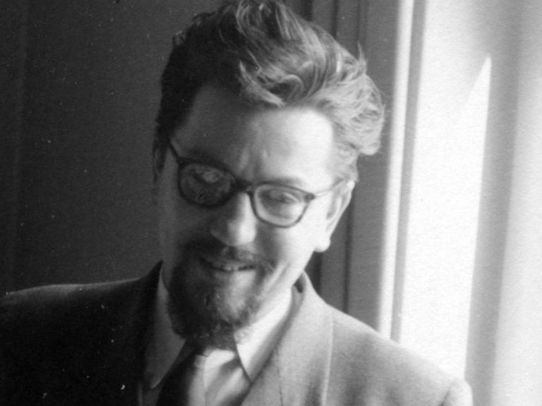 Der Komponist Bernd Alois Zimmermann steht vor einem Fenster, raucht und lächelt.