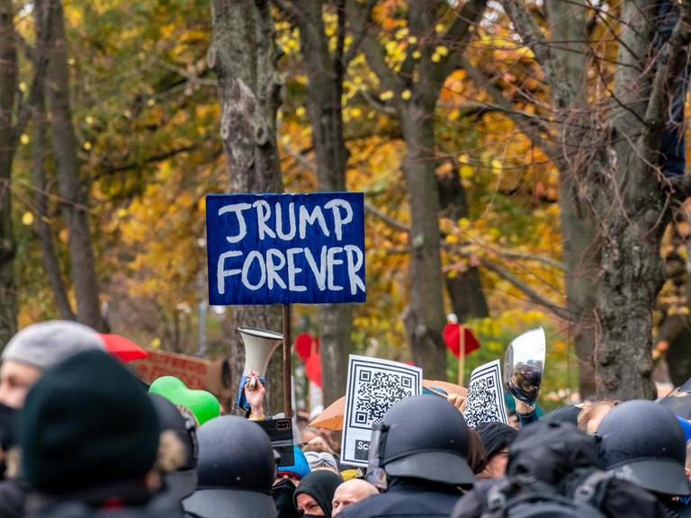 Nicht genehmigte Demonstration der Querdenken-Bewegung am. 18. November 2020 in Berlin. Vor einer herbstlichen Kulisse halten Demonstranten ein Schild "Trump forever" in die Höhe.