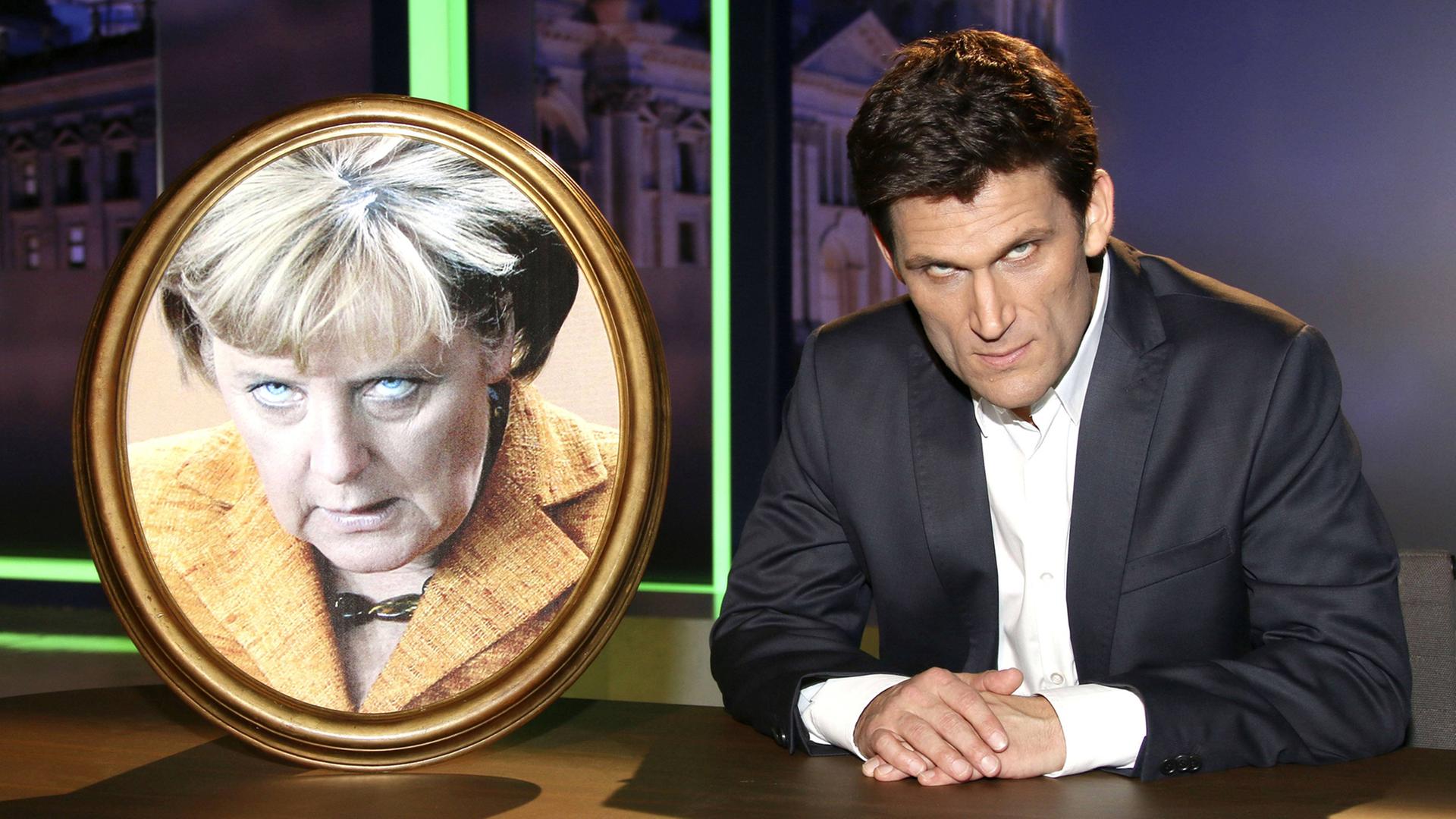 Christian Ehring beim Fototermin zur NDR-Satireshow extra 3 im NDR Studio 3. Hamburg, am 08.10.2014, neben einem Foto von Merkel, auf dem sie sehr drohend guckt.