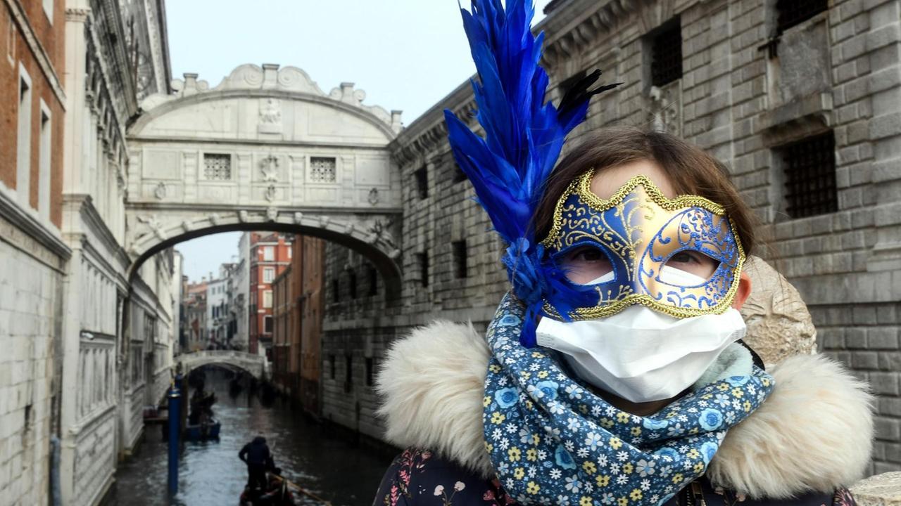 Ein junge Touristin trägt eine Schutzmaske und eine Karnevalsmaske bei ihrem Besuch in Venedig während der üblichen Zeit der Karnevalsfeierlichkeiten. Ein junge Touristin trägt eine Schutzmaske und eine Karnevalsmaske bei ihrem Besuch in Venedig während der üblichen Zeit der Karnevalsfeierlichkeiten.