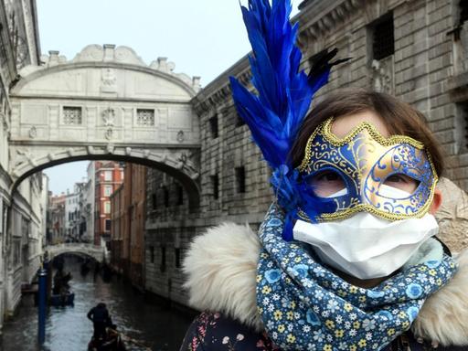 Ein junge Touristin trägt eine Schutzmaske und eine Karnevalsmaske bei ihrem Besuch in Venedig während der üblichen Zeit der Karnevalsfeierlichkeiten.