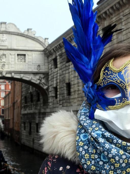 Ein junge Touristin trägt eine Schutzmaske und eine Karnevalsmaske bei ihrem Besuch in Venedig während der üblichen Zeit der Karnevalsfeierlichkeiten.