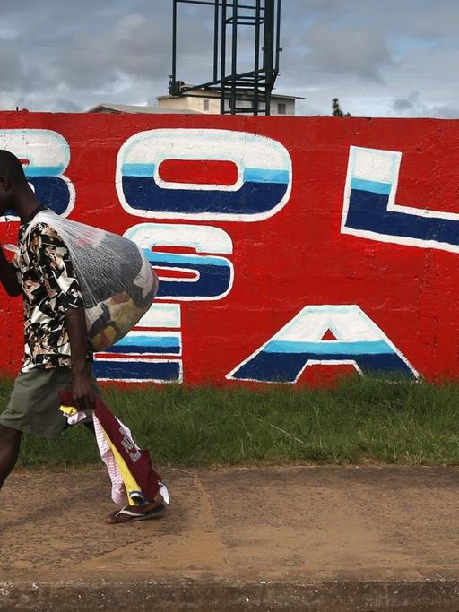 Ein Mann geht an einer Wand vorbei auf der "Ebola is real" geschrieben steht.