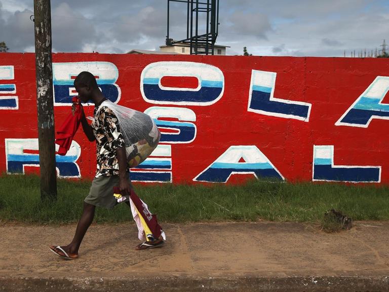 Ein Mann geht an einer Wand vorbei auf der "Ebola is real" geschrieben steht.