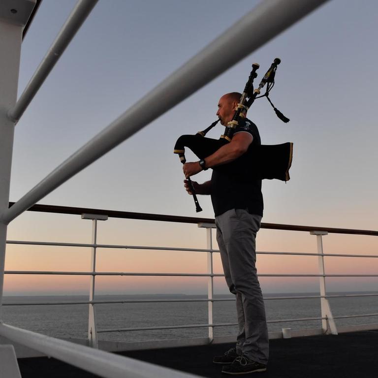 Ein Dudelsackspieler am Bord des britischen Kreuzfahrtschiffs RMS Queen Mary 2 im Atlantik Ein Dudelsackspieler am Bord des britischen Kreuzfahrtschiffs RMS Queen Mary 2 im Atlantik