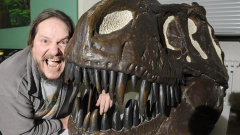 Saurierforscher Eberhard "Dino" Frey mit weit aufgerissenem Mund neben einem Schädelabguss eines Tyrannosaurus rex.