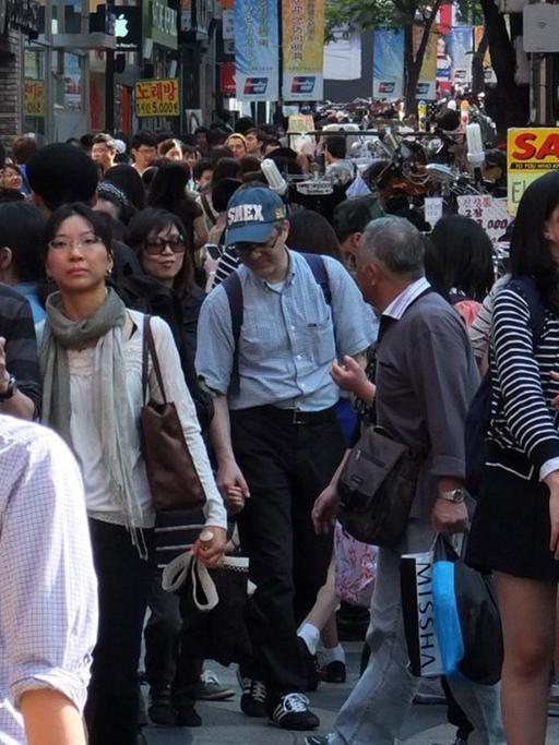 Zahlreiche Menschen strömen durch eine Einkaufsstraße in Myeongdong