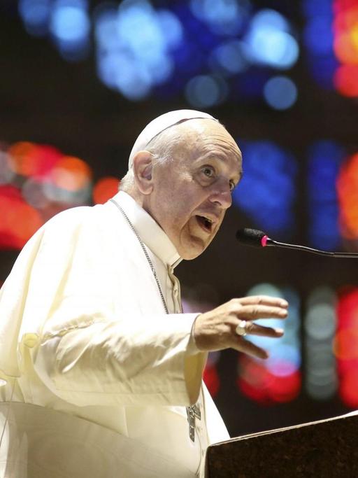 Papst Franziskus an einem Rednerpult, im Hintergrund bunte Lichter