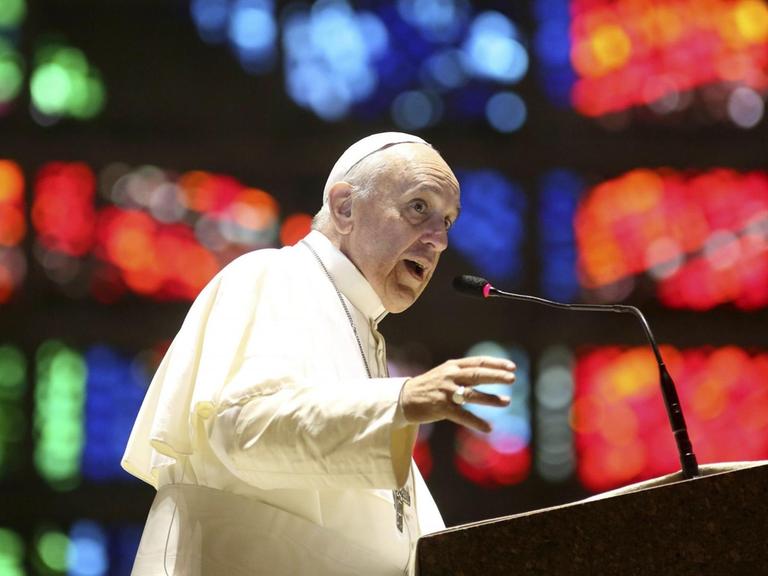Papst Franziskus an einem Rednerpult, im Hintergrund bunte Lichter