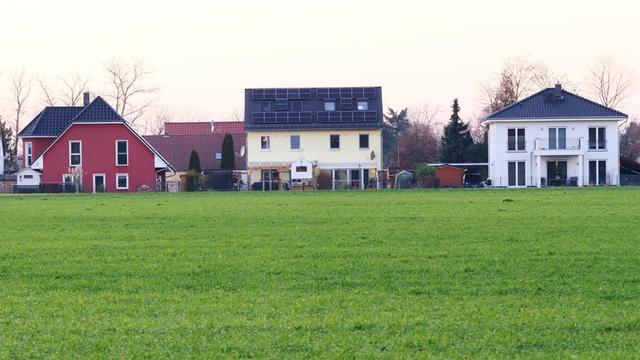 Neue Einfamilienhaeuser stehen an einer grünen Wiese in Feldrandlage bei Grossbeeren in Brandenburg.