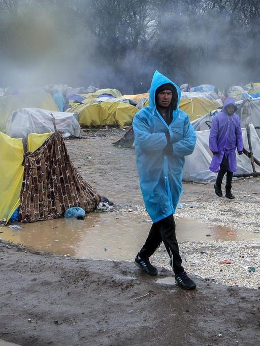 Zwei Männer im Regenponcho gehen durch ein notdürftiges Zeltlager von Flüchtlingen.
