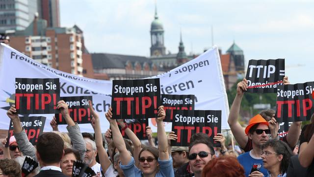 Demonstranten halten bei einer Wahlkampfveranstaltung der CDU auf dem Hamburger Fischmarkt ein Plakat mit der Aufschrift "Stoppen Sie TTIP" in die Höhe.