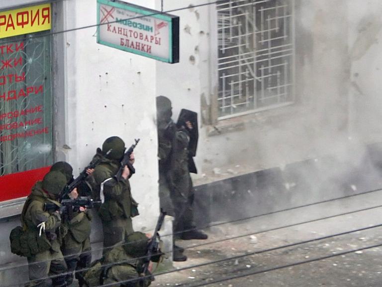 Polizisten einer Spezialeinheit vor einem vergitterten Fenster in der nordkaukasischen Stadt Naltschik, aus dem Rauchschwaden austreten.