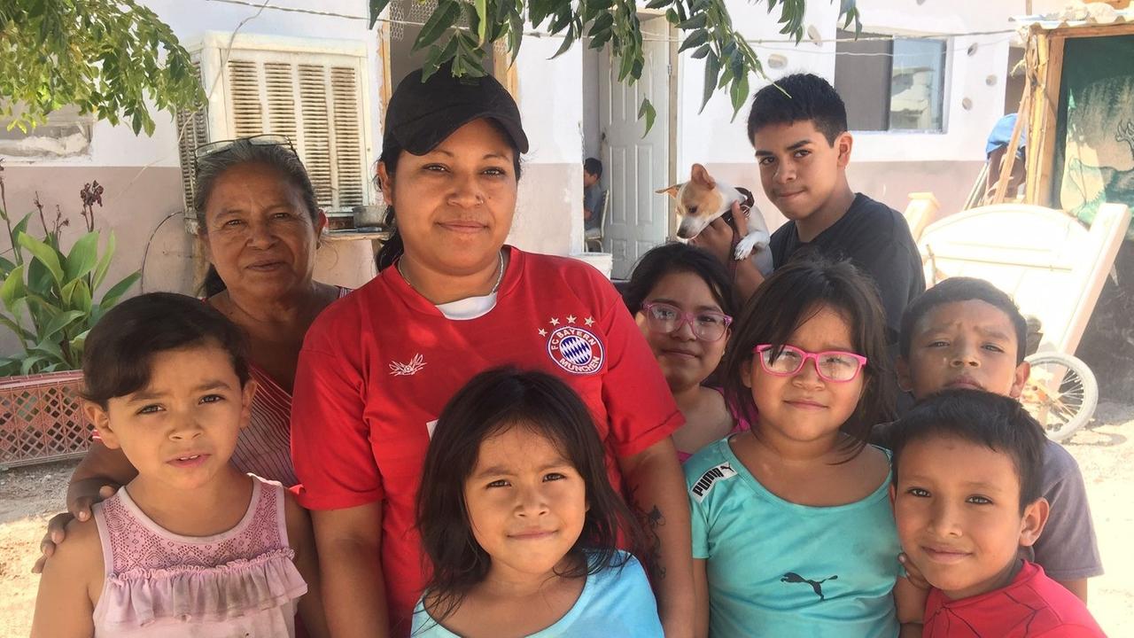 Gruppenbild der Arbeiterin Cinthia Mora im roten T-Shirt mit dem Logo des FC Bayern München und ihren Kindern. Gruppenbild der Arbeiterin Cinthia Mora im roten T-Shirt mit dem Logo des FC Bayern München und ihren Kindern.